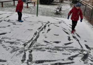 Chłopcy robią ślady na śniegu na boisku.
